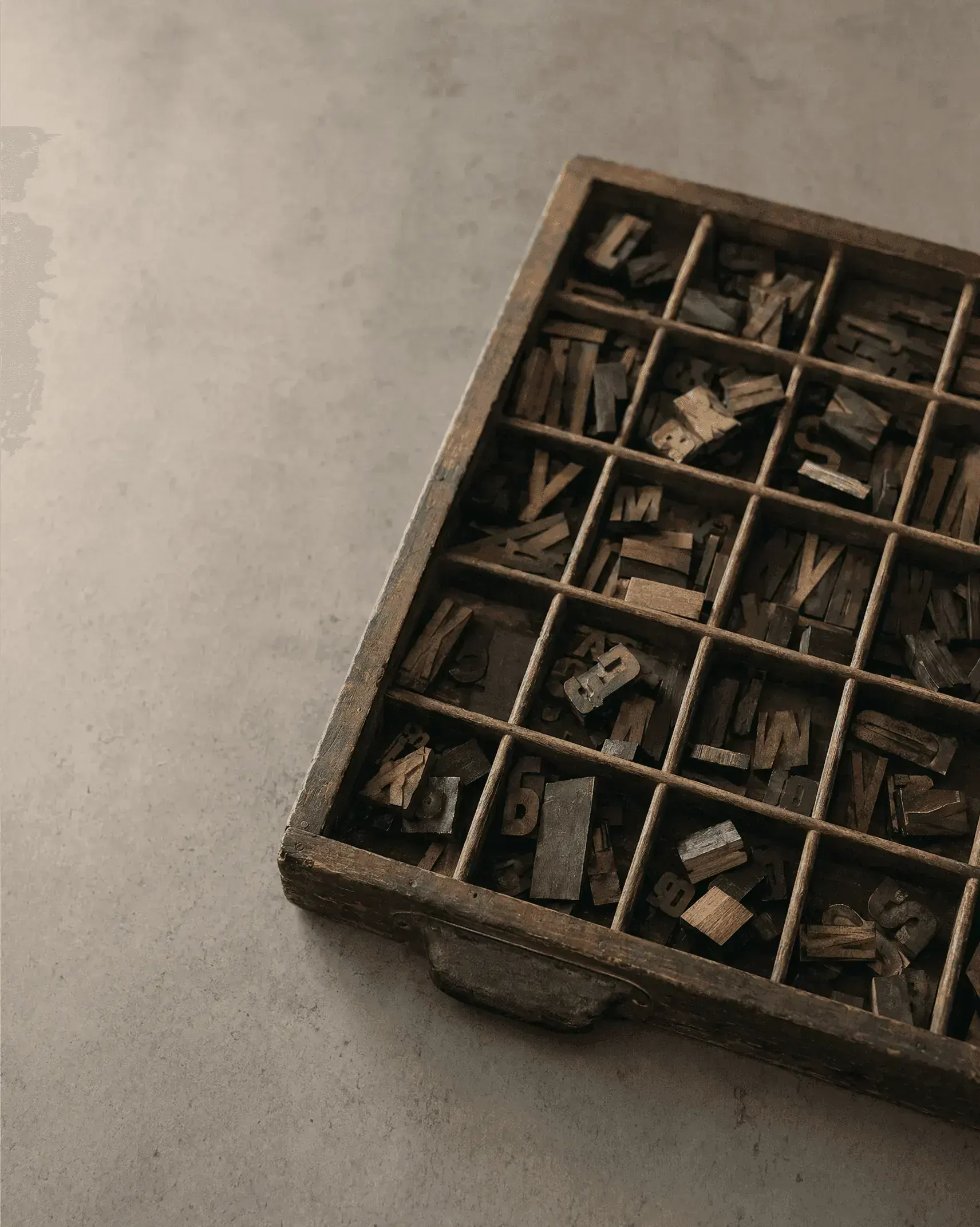 A printer's wooden type case holding loose letterpress capitals in warm afternoon light.
