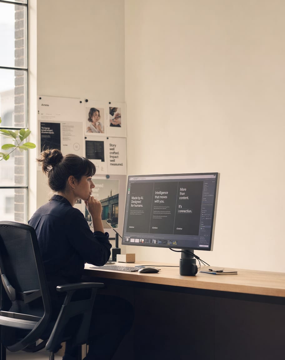 A strategist reviewing campaign copy variations on a calibrated monitor beside printed proofs.