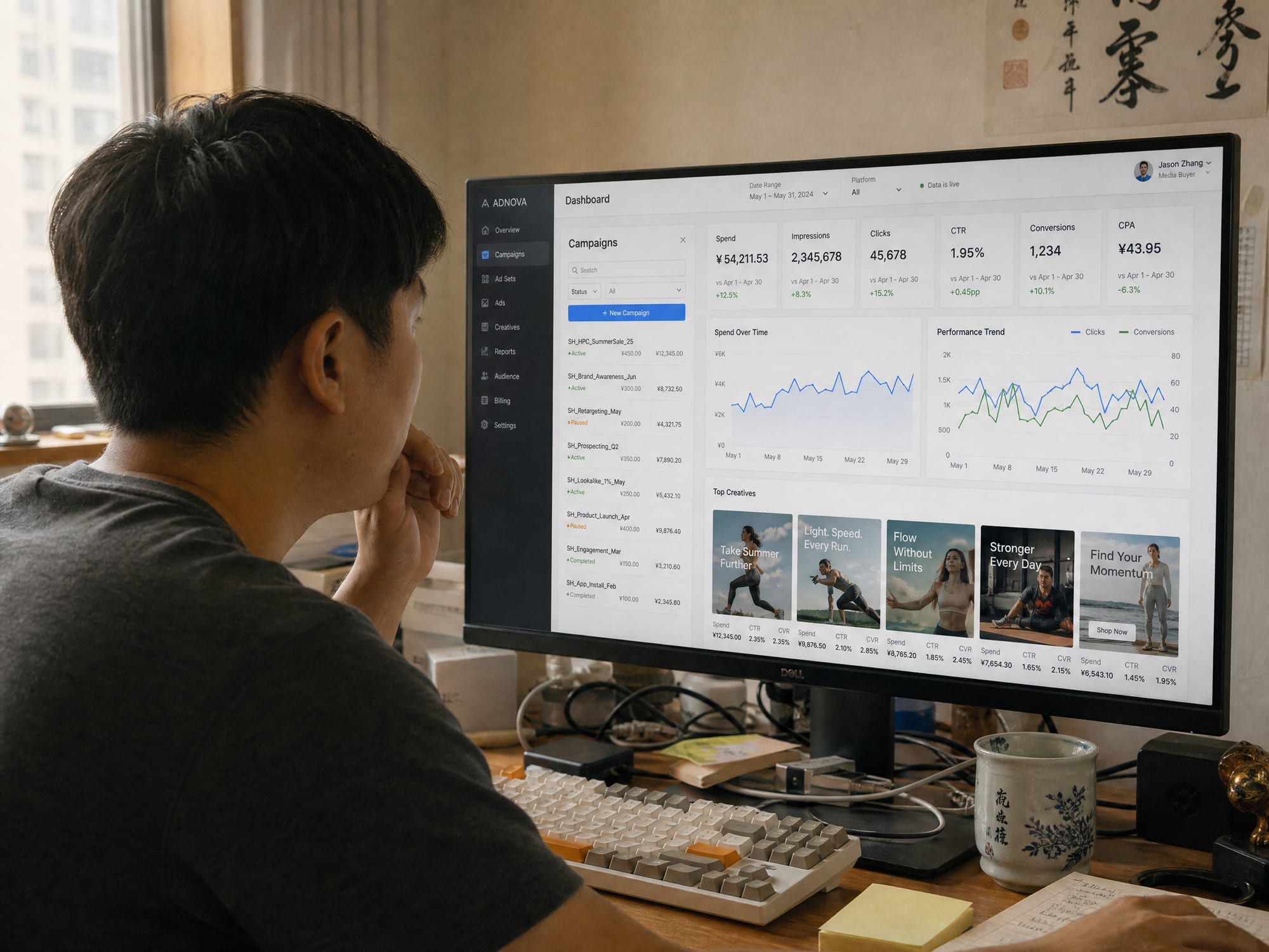 A media buyer at a daylit studio desk, the calibrated monitor showing the Amazon advertising console campaign dashboard with Sponsored Brands and Sponsored Display placements live.