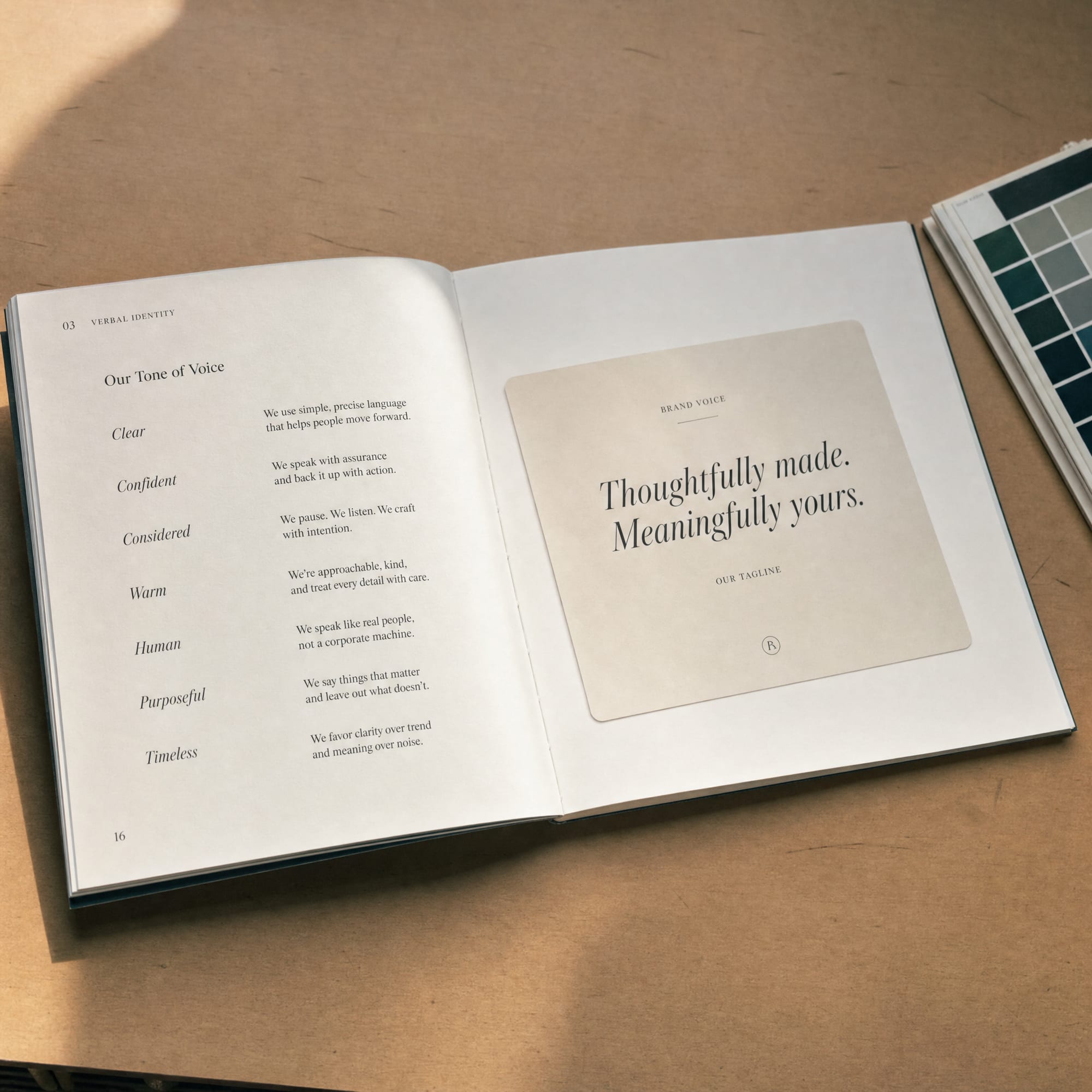 A printed brand book opened to a verbal-identity spread on a warm worktable, with a small colour chip book at the edge.