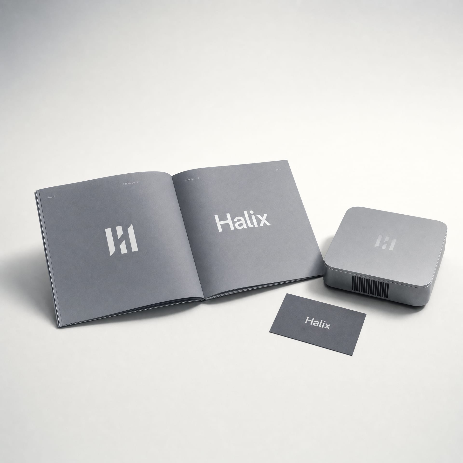 A cool-grey Halix brand book opened to a monogram spread beside an anodized aluminium device on a studio table.