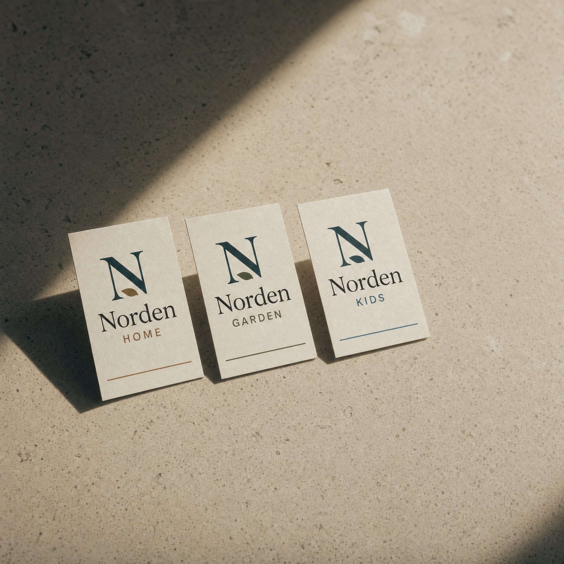 Three printed identity cards for Norden Home, Norden Garden and Norden Kids sharing the same monogram device.