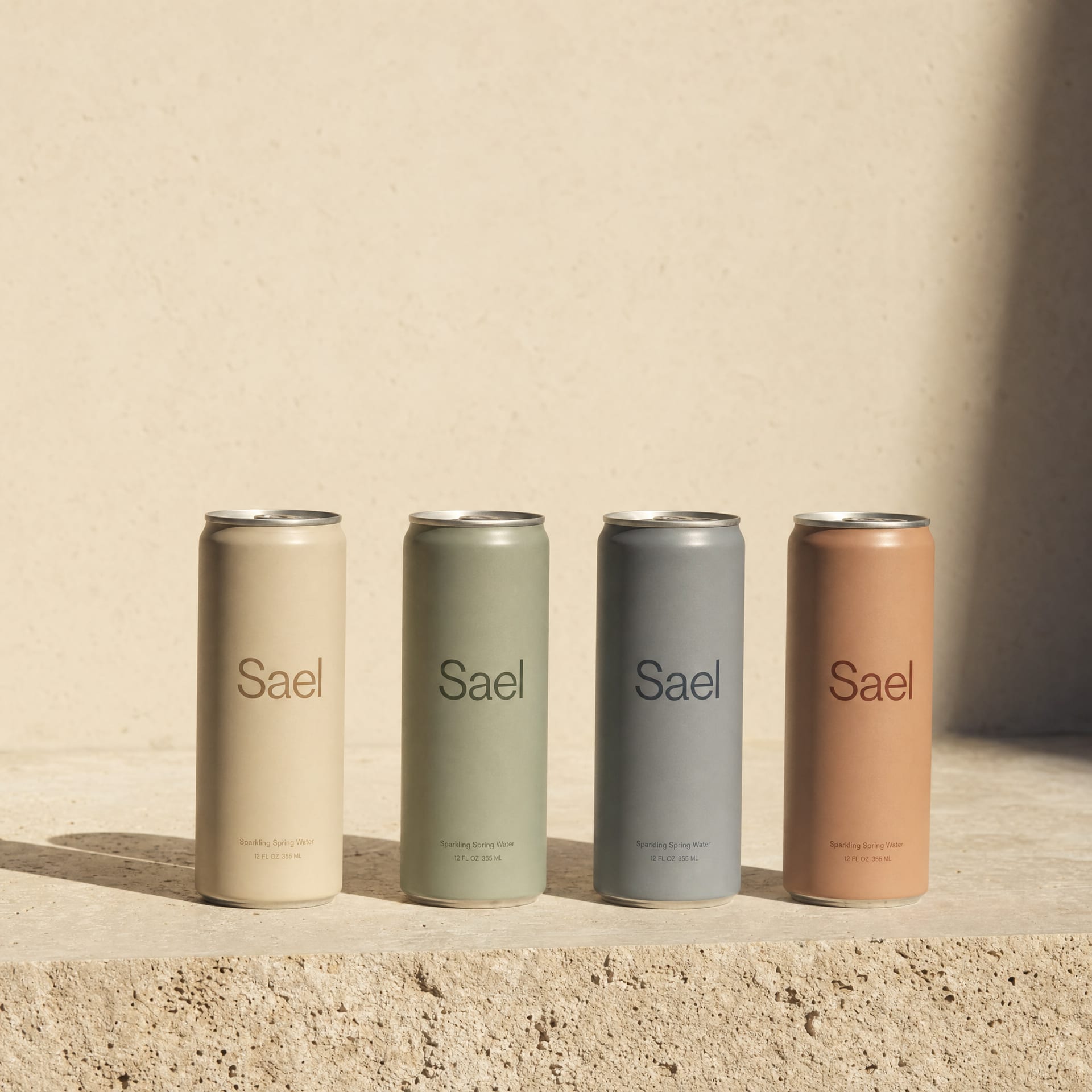 Four aluminium cans in a row carrying the Sael wordmark in four secondary palette tones, on travertine.