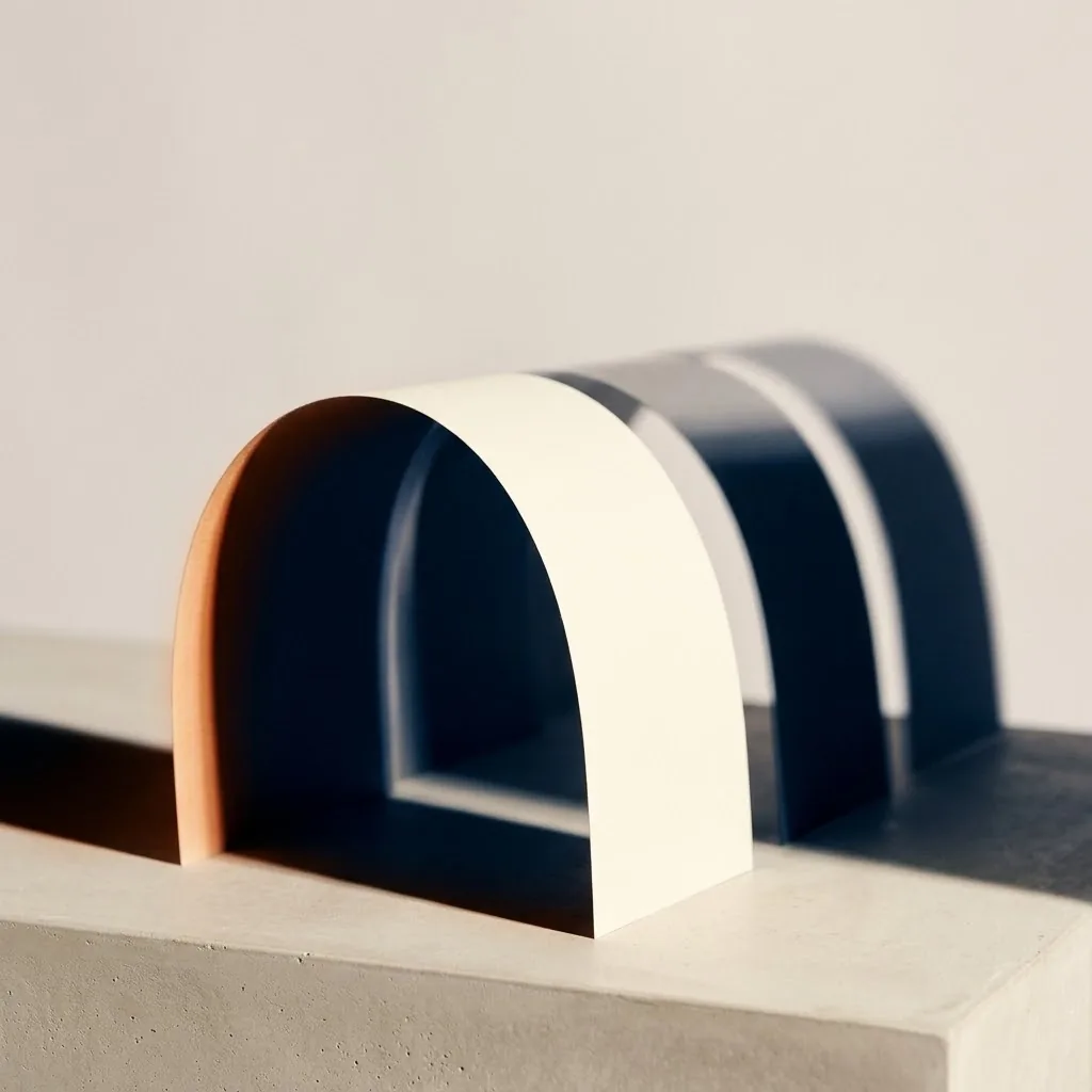 Sculptural paper arches in cream, navy, and burnt-orange on a concrete plinth.