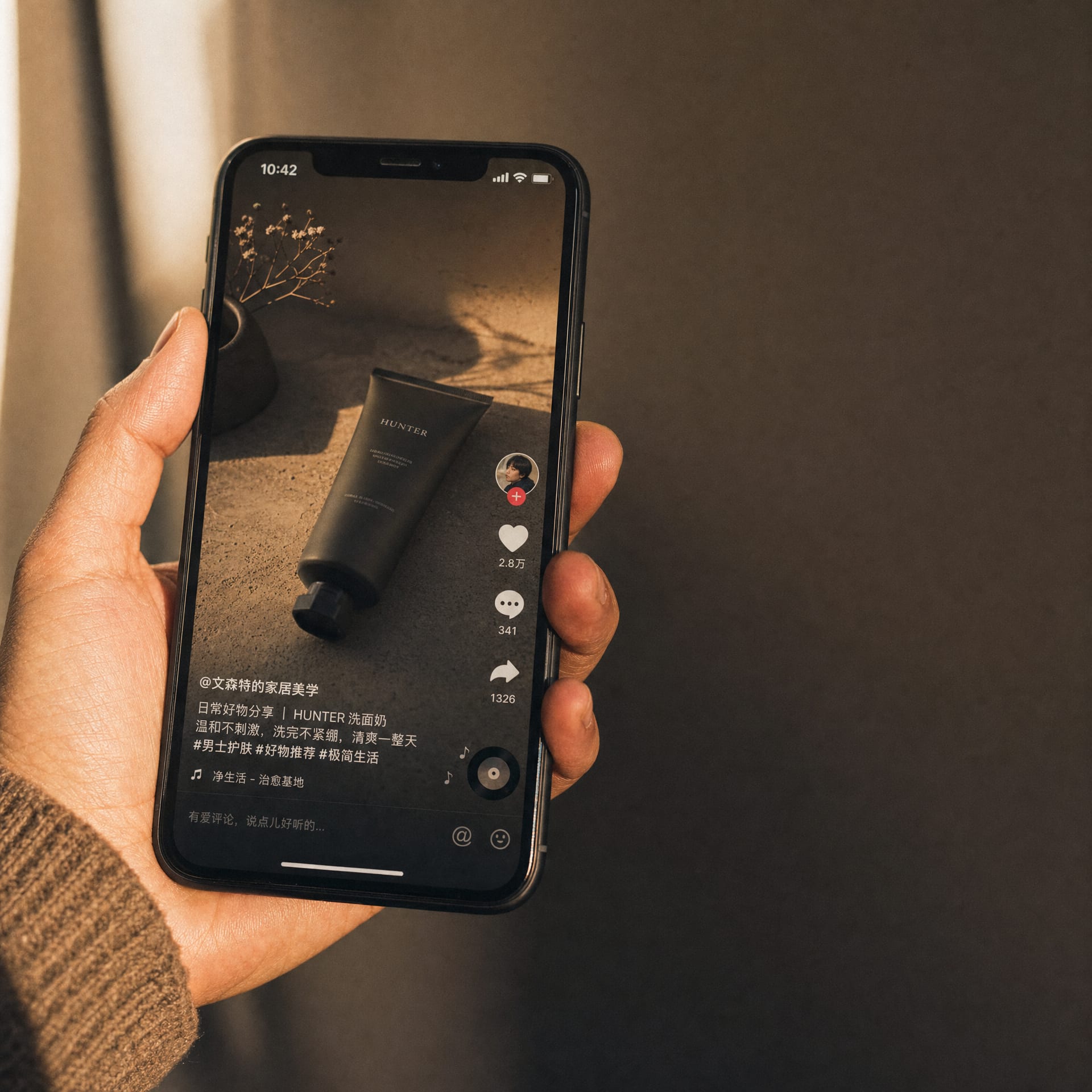 A hand holding a phone in warm rim light showing a paused vertical Douyin video.