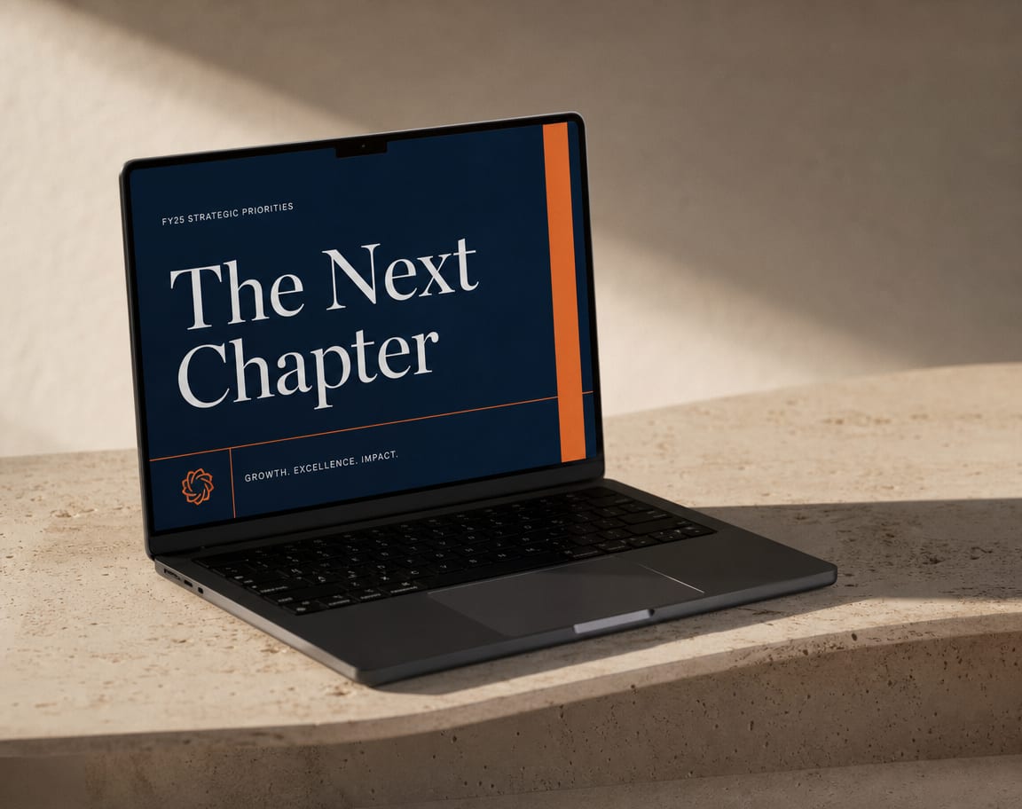 A dark slate laptop on a travertine surface showing a clean pitch deck title slide in deep navy with a warm orange accent.