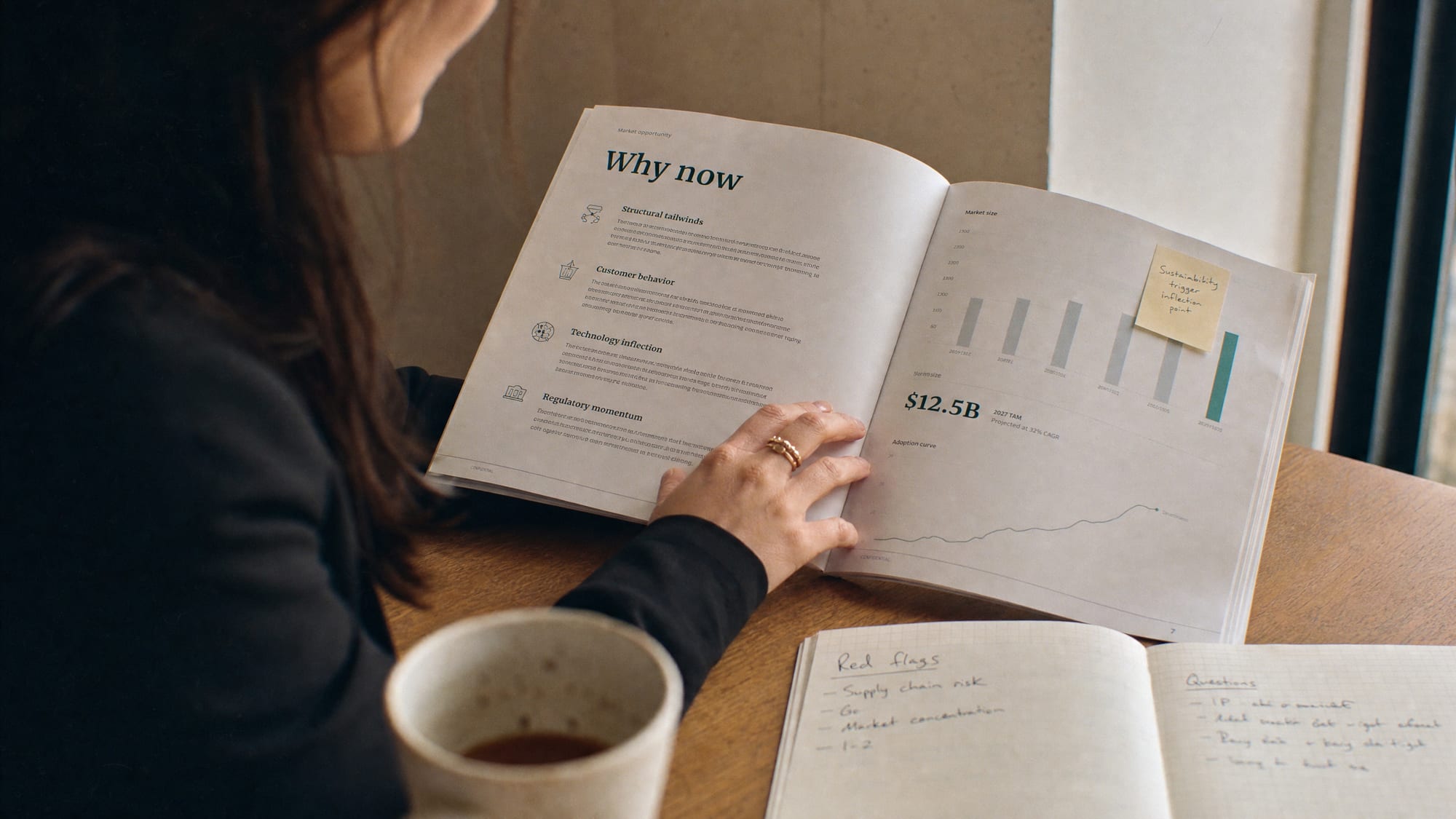 An investor at a desk reviewing a printed pitch deck, coffee cup beside it, half-frame on the slide and half on her face.