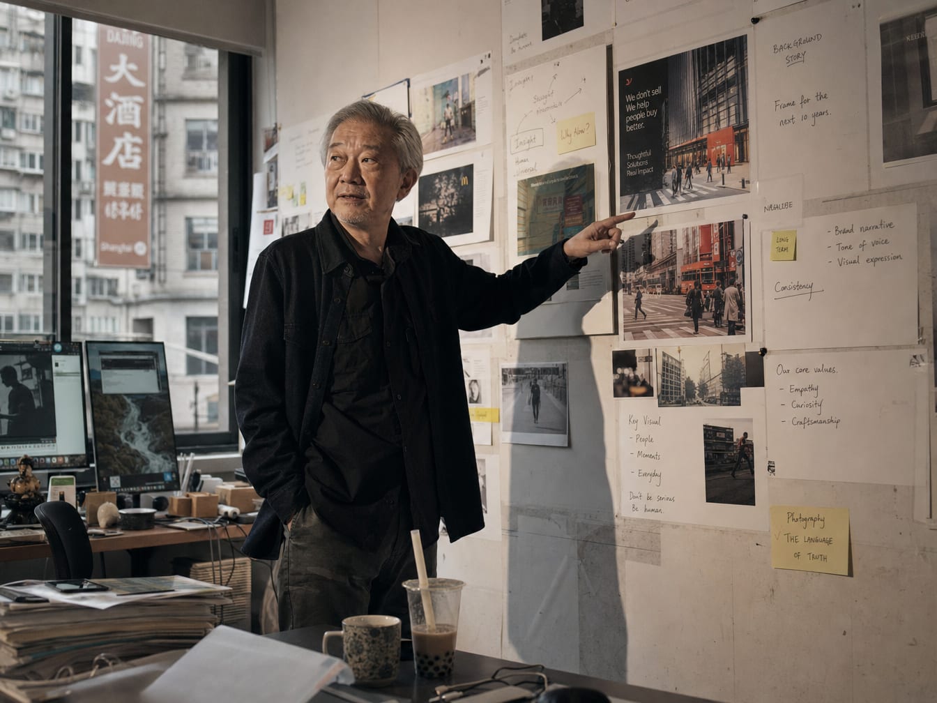 A senior creative director in front of a wall of pinned printed ad frames, pointing at one.