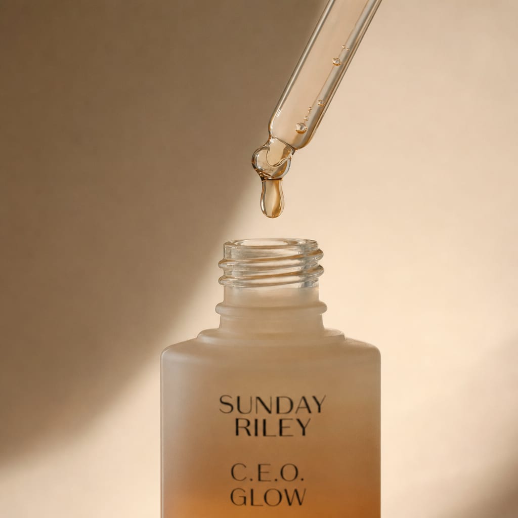 A close studio frame of a serum dropper releasing a golden bead, lit by one soft window source.