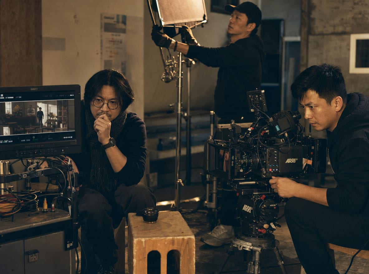 A director watching the live monitor on a film set, DOP behind the cinema camera, gaffer adjusting a flag.
