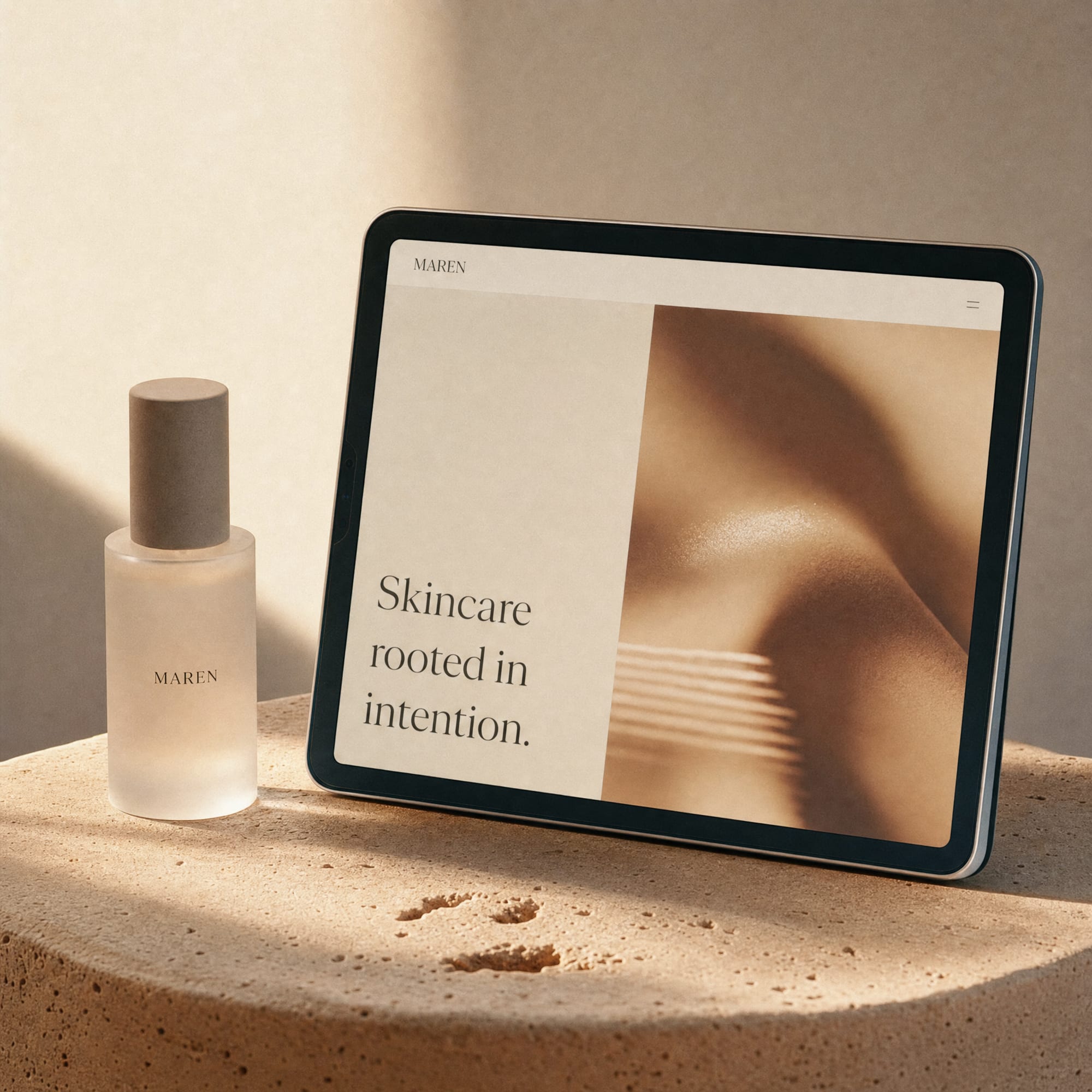A tablet on warm ceramic beside a frosted bottle, displaying a Maren beauty homepage with a soft hero image and serif headline.