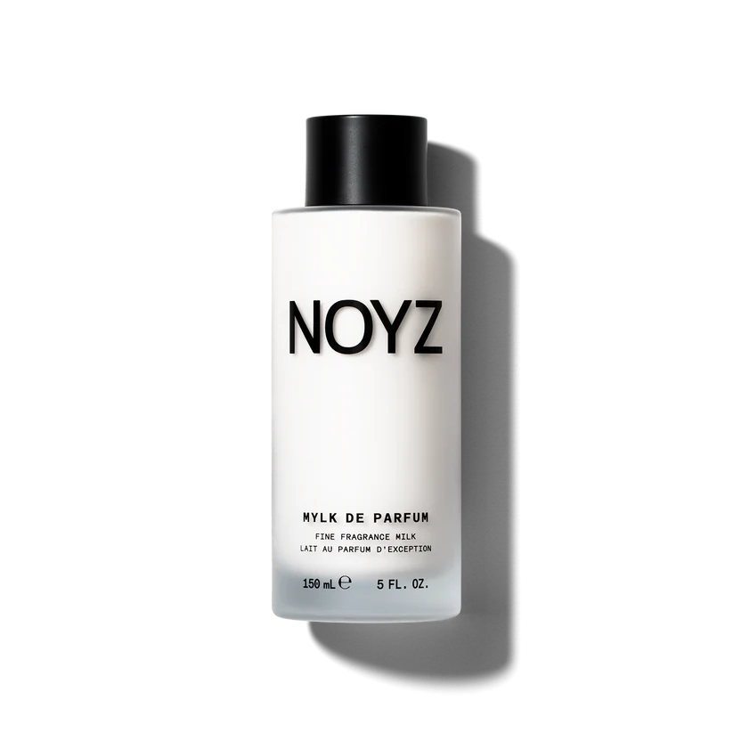 A diffused spray of perfume mist softening into a creamy milk texture against a warm neutral backdrop for the Noyz Mylk de Parfum launch.
